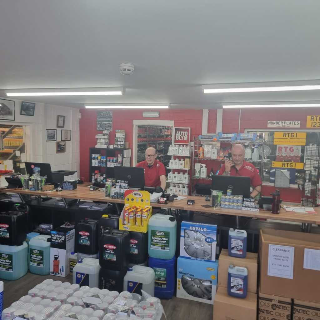 Two men standing behind a counter in a store they are surround by car parts and products